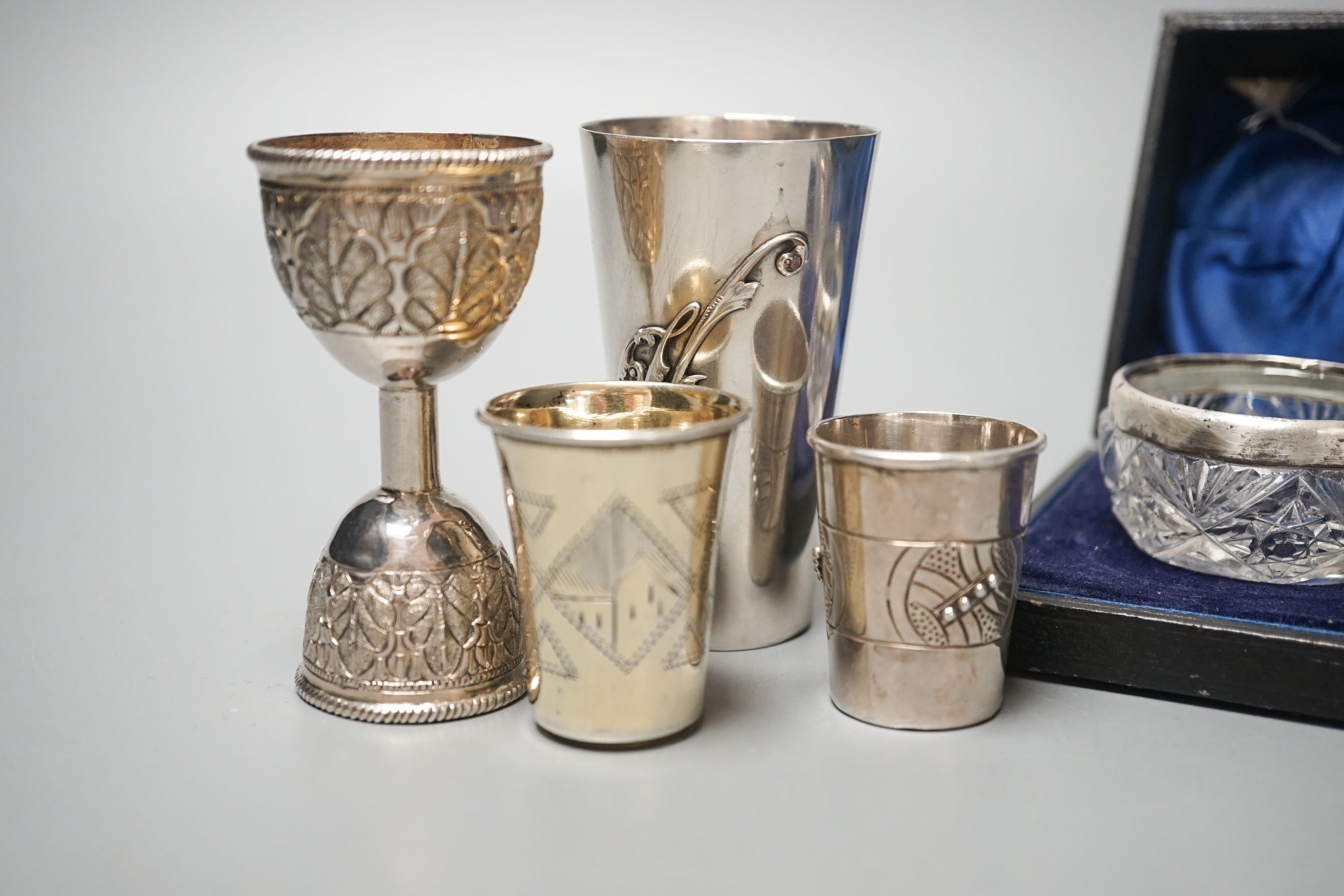 Two early 20th century Russian white metal tots, a sterling beaker, white metal double measure and a case pair of silver mounted glass salts.